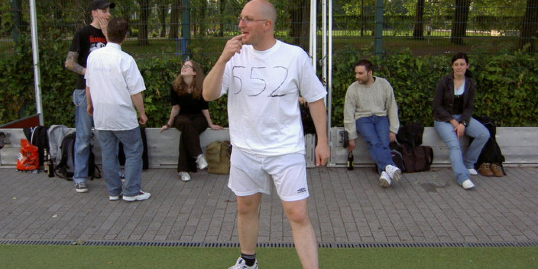 Menschen auf dem Fußballplatz. Ein Mensch in weiß pfeifft ein Spiel an.