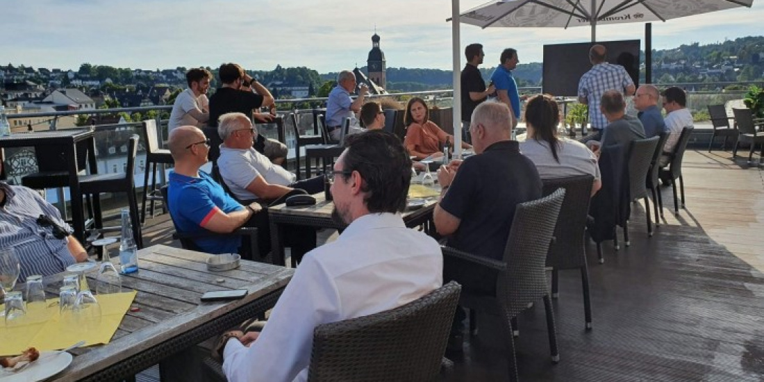 Menschen im Tageslicht auf einer Dachterasse unter Sonnenschirmen