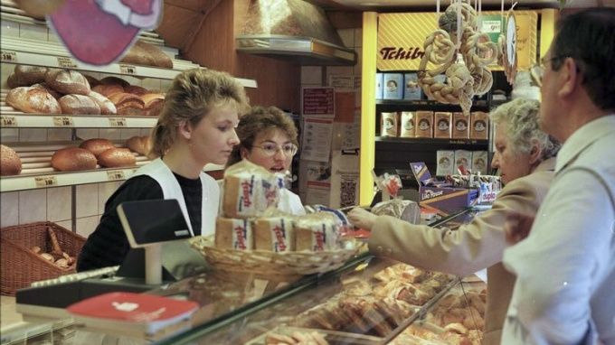 In einer Bäckerei stehen zwei Verkäuferinnen durch einen Tresen getrennt zwei Kunden gegenüber.
